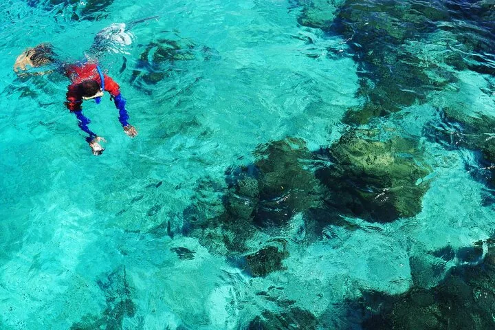 Persona haciendo esnórquel nadando en aguas turquesas cristalinas sobre formaciones de coral